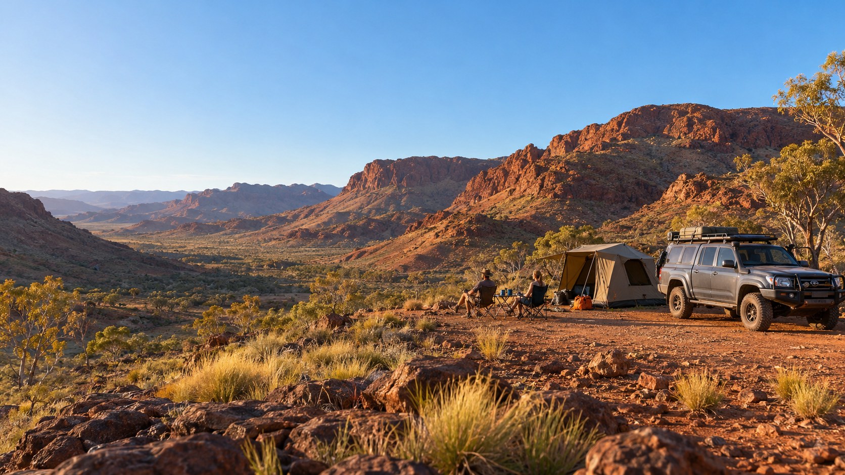 Two people in camping chairs beside a canvas tent and a loaded four-wheel drive, looking out over a red-rock valley
